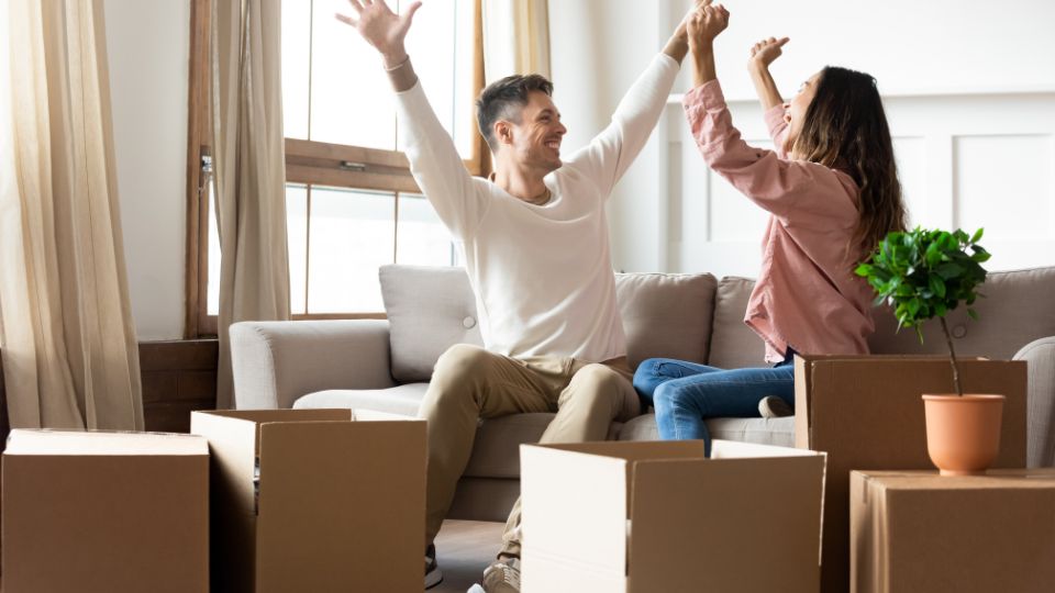 two very happy renters throwing their arms up in the air surrounded by moving boxes